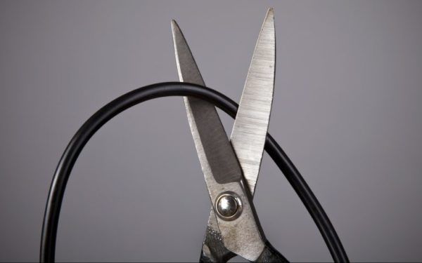 Scissors cutting a computer wire on gray background (wireless or blackout concept)