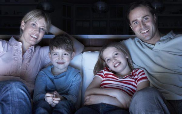 Family Watching TV At Night Sitting On Sofa Together