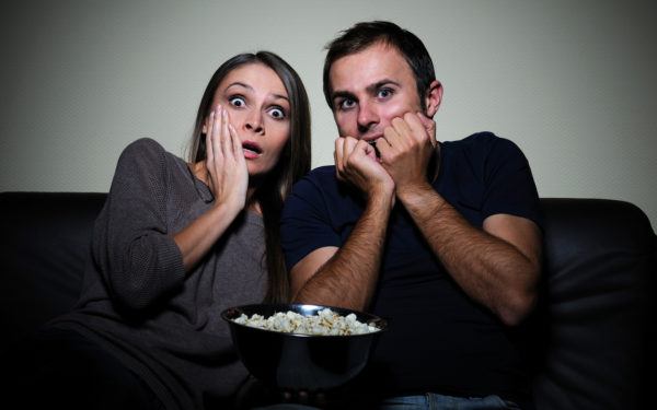 Young couple sitting on a sofa watching scary movie on tv