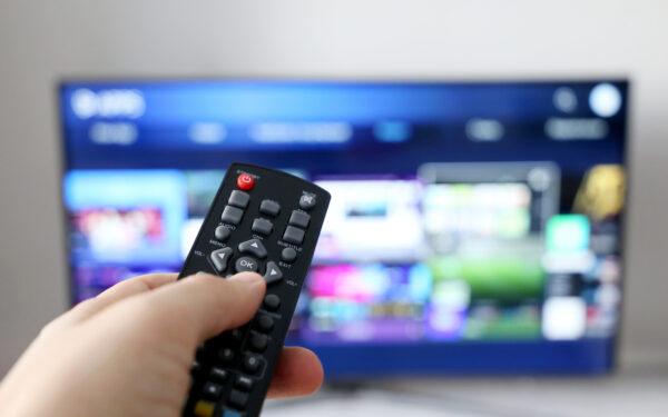 Hand holding a remote control in front of a TV
